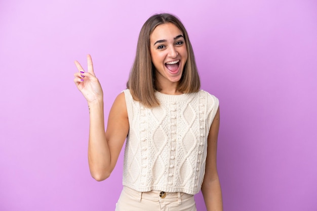 Joven mujer caucásica aislada sobre fondo púrpura sonriendo y mostrando el signo de la victoria