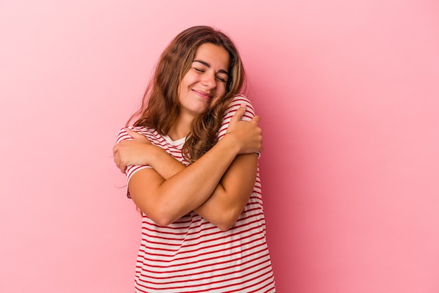 Foto joven mujer caucásica aislada sobre fondo rosa abrazos, sonriendo despreocupada y feliz.