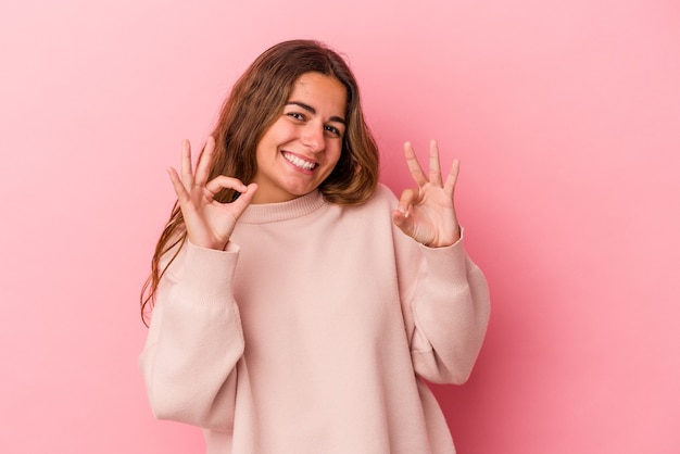 Joven mujer caucásica aislada sobre fondo rosa alegre y confiado mostrando gesto ok.