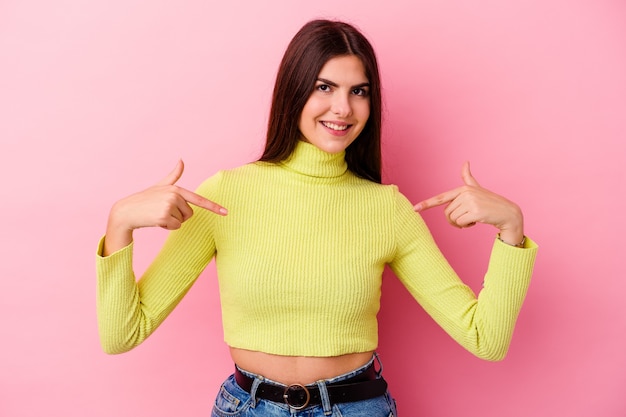 Joven mujer caucásica aislada sobre fondo rosa apunta hacia abajo con los dedos, sentimiento positivo.