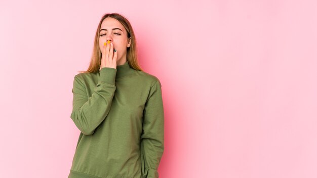 Joven mujer caucásica aislada sobre fondo rosa bostezando mostrando un gesto cansado cubriendo la boca con la mano.