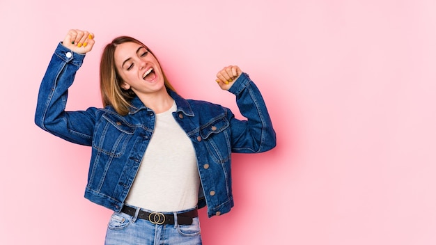 Joven mujer caucásica aislada sobre fondo rosa celebrando un día especial, salta y levanta los brazos con energía.