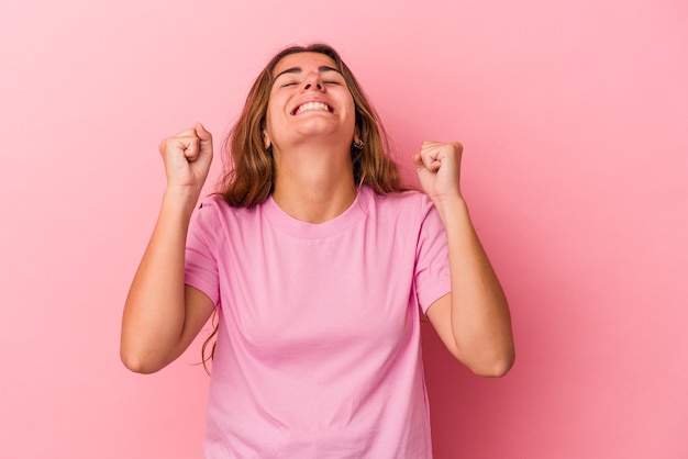 Joven mujer caucásica aislada sobre fondo rosa celebrando una victoria, pasión y entusiasmo, expresión feliz.