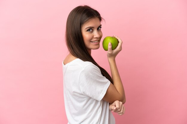 Joven mujer caucásica aislada sobre fondo rosa comiendo una manzana