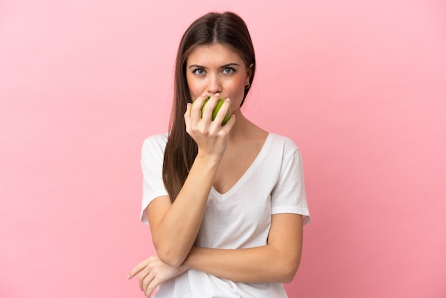 Joven mujer caucásica aislada sobre fondo rosa comiendo una manzana
