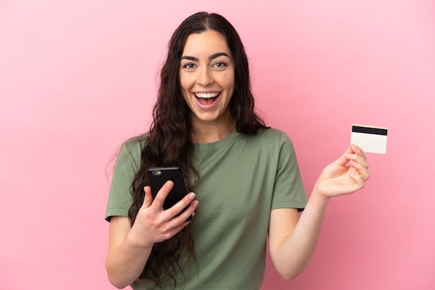 Joven mujer caucásica aislada sobre fondo rosa comprando con el móvil