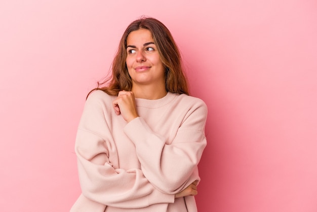 Joven mujer caucásica aislada sobre fondo rosa confundida, se siente dudosa e insegura.