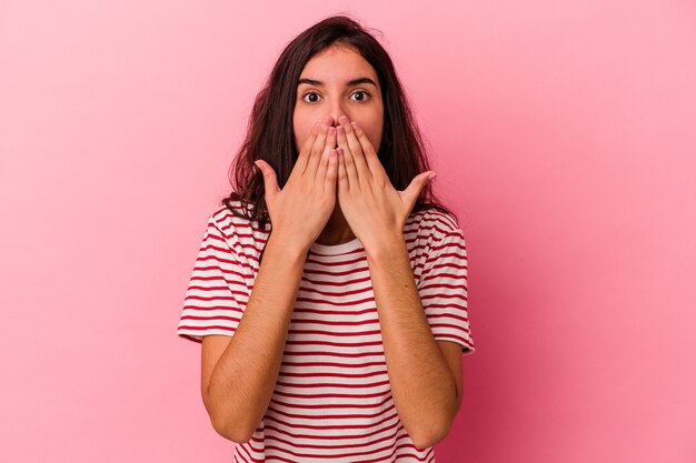 Joven mujer caucásica aislada sobre fondo rosa conmocionada, tapándose la boca con las manos, ansiosa por descubrir algo nuevo.