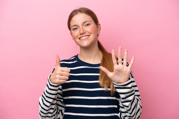 Joven mujer caucásica aislada sobre fondo rosa contando seis con los dedos