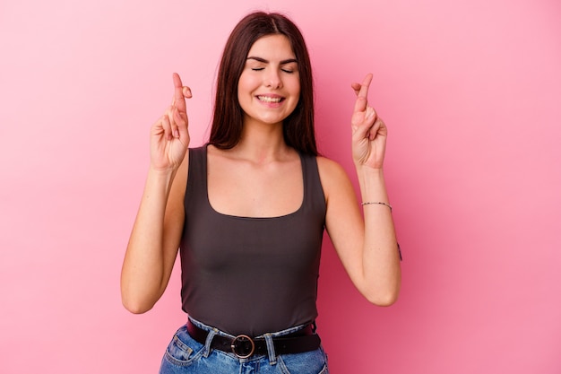 Joven mujer caucásica aislada sobre fondo rosa cruzando los dedos para tener suerte