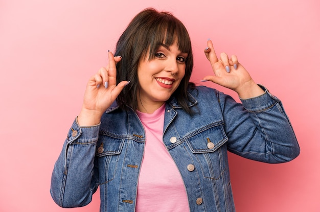 Joven mujer caucásica aislada sobre fondo rosa cruzando los dedos para tener suerte