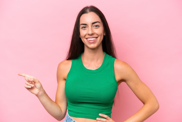 Joven mujer caucásica aislada sobre fondo rosa dedo acusador hacia el lado