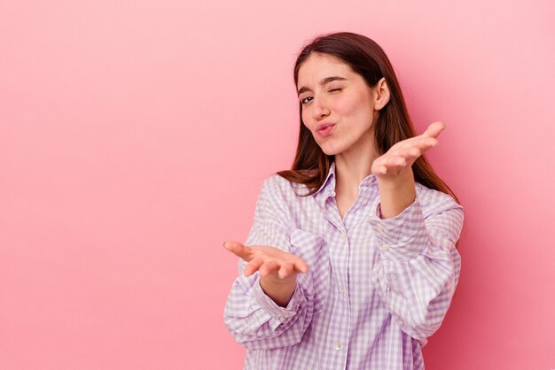 Joven mujer caucásica aislada sobre fondo rosa doblando los labios y sosteniendo las palmas para enviar beso al aire.