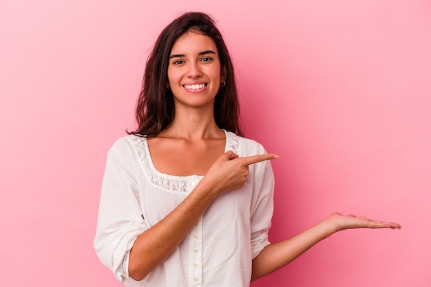 Joven mujer caucásica aislada sobre fondo rosa emocionada sosteniendo un espacio de copia en la palma.