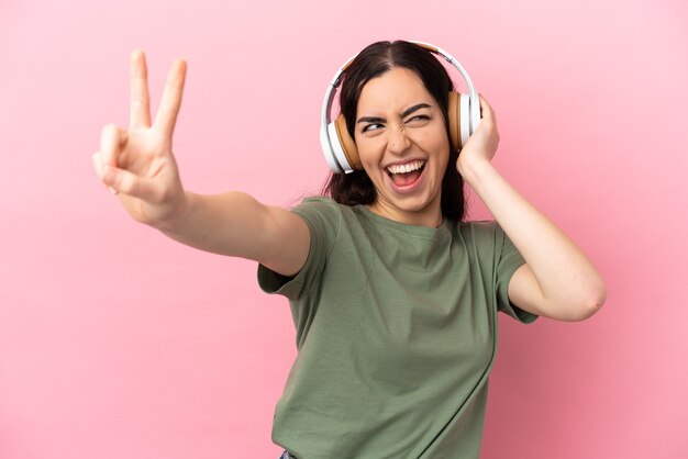 Joven mujer caucásica aislada sobre fondo rosa escuchando música y cantando