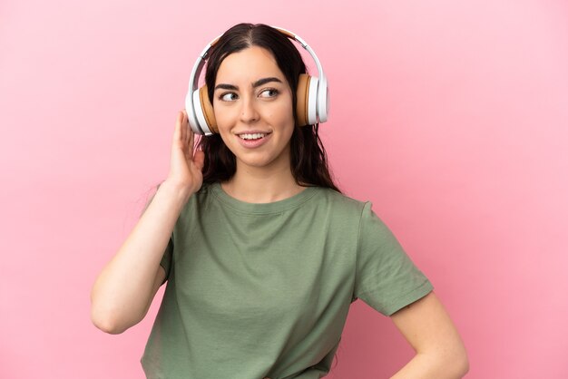 Joven mujer caucásica aislada sobre fondo rosa escuchando música
