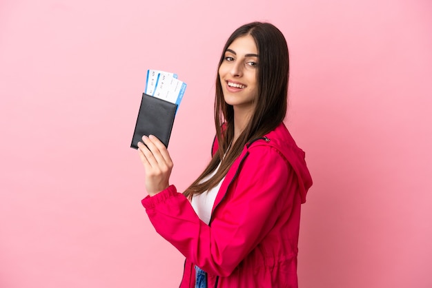 Joven mujer caucásica aislada sobre fondo rosa feliz de vacaciones con pasaporte y billetes de avión