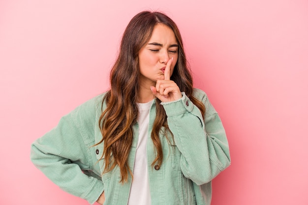 Joven mujer caucásica aislada sobre fondo rosa guardando un secreto o pidiendo silencio.