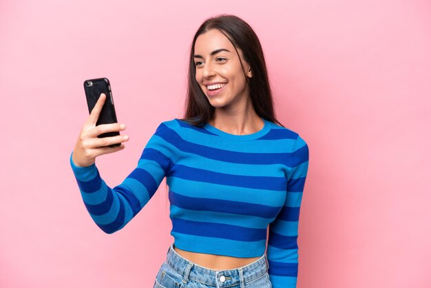 Joven mujer caucásica aislada sobre fondo rosa haciendo un selfie