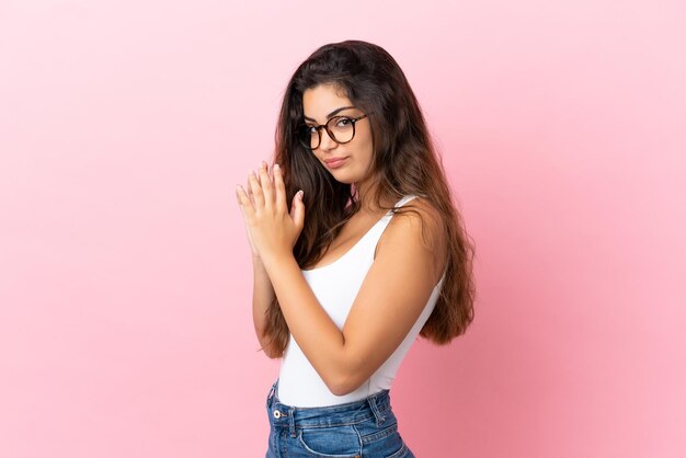 Joven mujer caucásica aislada sobre fondo rosa intrigando algo