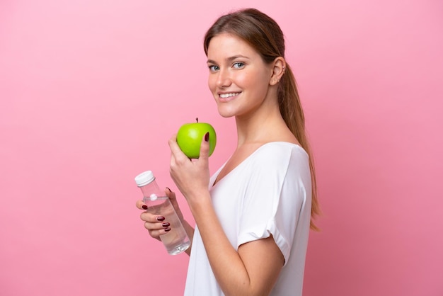 Joven mujer caucásica aislada sobre fondo rosa con una manzana y con una botella de agua