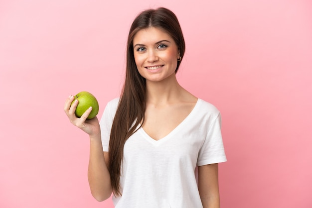 Joven mujer caucásica aislada sobre fondo rosa con una manzana