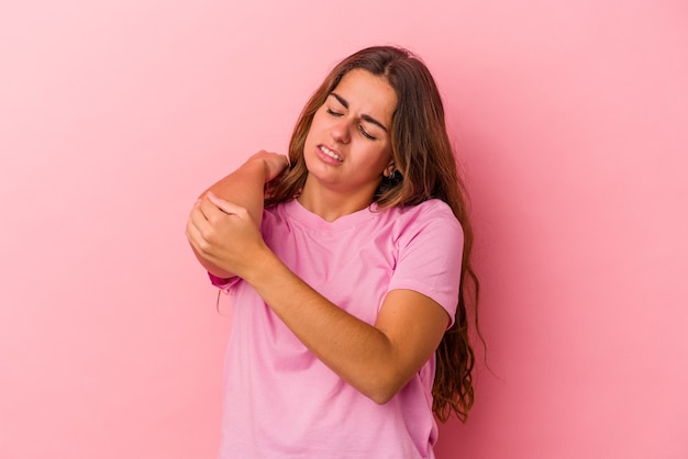 Joven mujer caucásica aislada sobre fondo rosa masajeando el codo, sufriendo después de un mal movimiento.