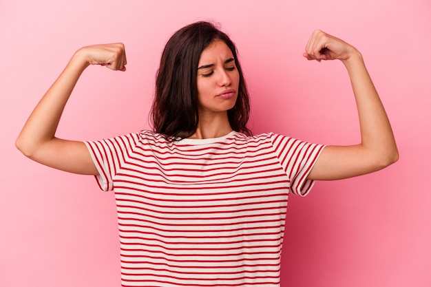 Joven mujer caucásica aislada sobre fondo rosa mostrando gesto de fuerza con los brazos, símbolo del poder femenino