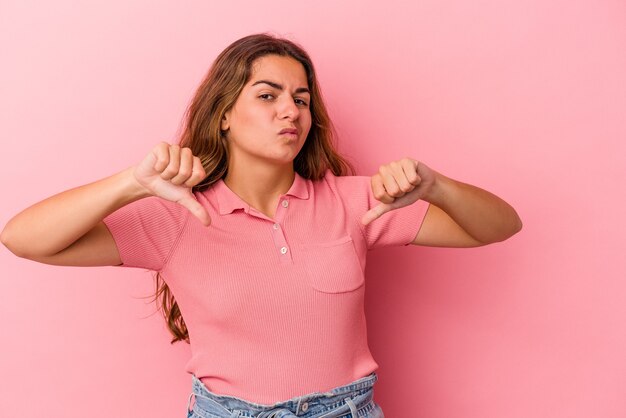 Joven mujer caucásica aislada sobre fondo rosa mostrando el pulgar hacia abajo, concepto de decepción.