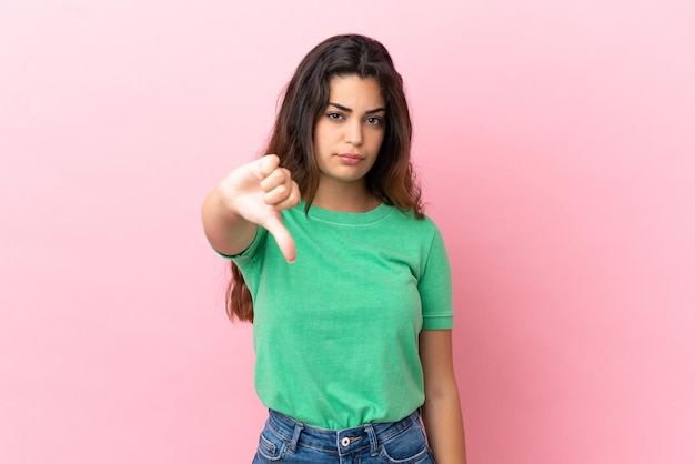 Joven mujer caucásica aislada sobre fondo rosa mostrando el pulgar hacia abajo con expresión negativa