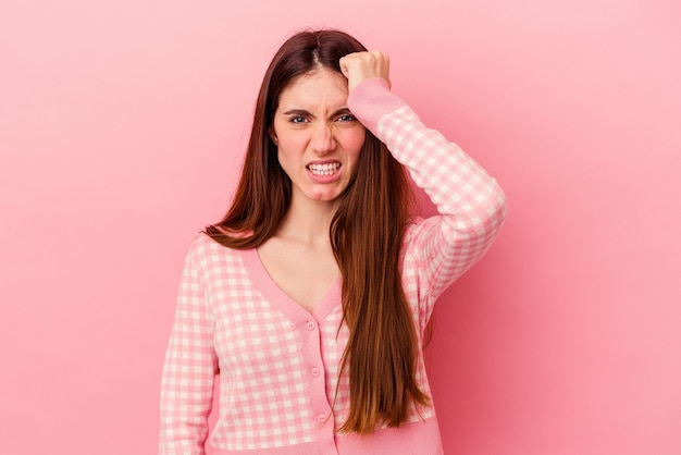 Joven mujer caucásica aislada sobre fondo rosa olvidando algo, golpeándose la frente con la palma y cerrando los ojos.