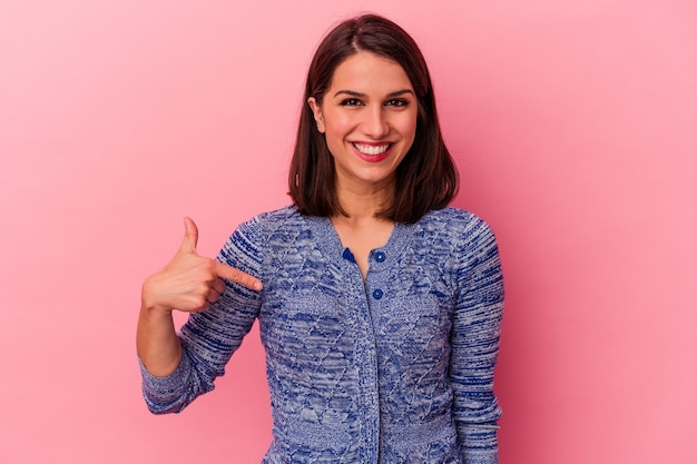 Joven mujer caucásica aislada sobre fondo rosa persona apuntando con la mano a un espacio de copia de camisa, orgulloso y seguro