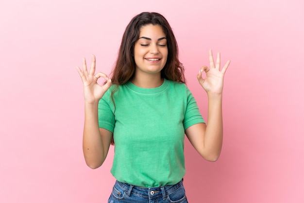 Joven mujer caucásica aislada sobre fondo rosa en pose zen