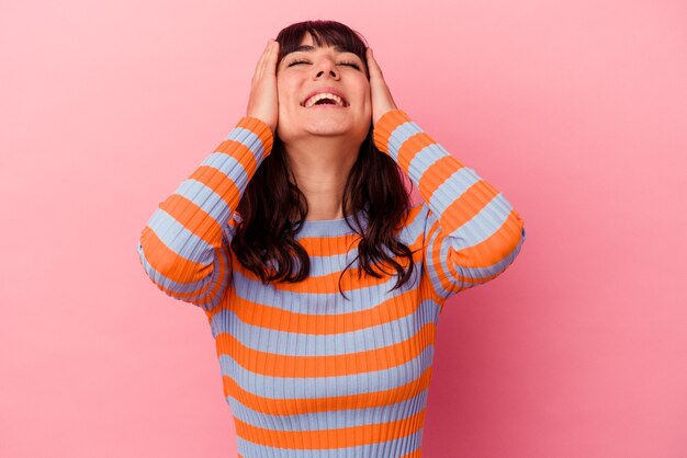 Joven mujer caucásica aislada sobre fondo rosa se ríe con alegría manteniendo las manos en la cabeza. Concepto de felicidad.