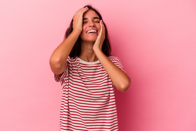 Joven mujer caucásica aislada sobre fondo rosa se ríe con alegría manteniendo las manos en la cabeza. Concepto de felicidad.