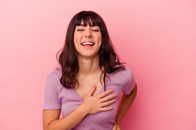 Joven mujer caucásica aislada sobre fondo rosa riendo manteniendo las manos en el corazón, concepto de felicidad.