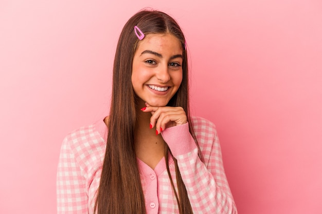 Joven mujer caucásica aislada sobre fondo rosa sonriendo feliz y seguro, tocando la barbilla con la mano.