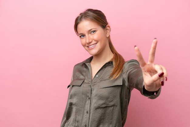 Foto joven mujer caucásica aislada sobre fondo rosa sonriendo y mostrando el signo de la victoria