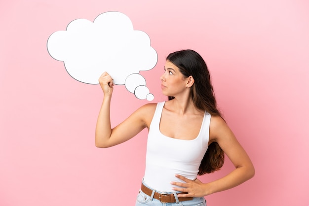 Joven mujer caucásica aislada sobre fondo rosa sosteniendo un bocadillo de diálogo de pensamiento