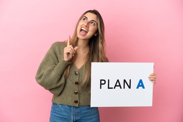 Joven mujer caucásica aislada sobre fondo rosa sosteniendo un cartel con el mensaje PLAN A y pensando