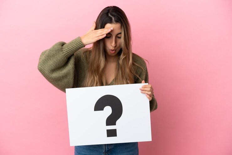 Foto joven mujer caucásica aislada sobre fondo rosa sosteniendo un cartel con el símbolo de signo de interrogación con expresión de sorpresa