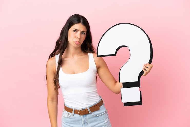 Foto joven mujer caucásica aislada sobre fondo rosa sosteniendo un icono de signo de interrogación y con expresión triste