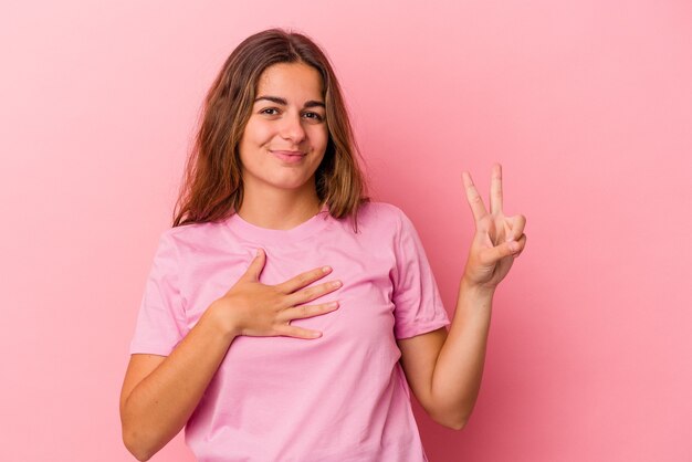 Joven mujer caucásica aislada sobre fondo rosa tomando un juramento, poniendo la mano en el pecho.