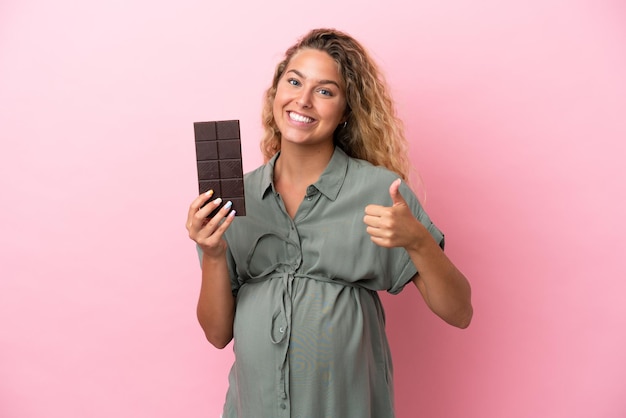 Joven mujer caucásica aislada sobre fondo rosa tomando una tableta de chocolate en una mano y una manzana en la otra