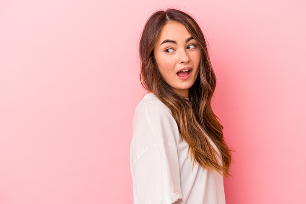 Joven mujer caucásica aislada sobre fondo rosa se ve a un lado sonriente, alegre y agradable.