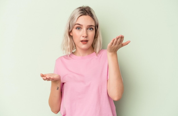 Joven mujer caucásica aislada sobre fondo verde hace escala con los brazos, se siente feliz y confiada.