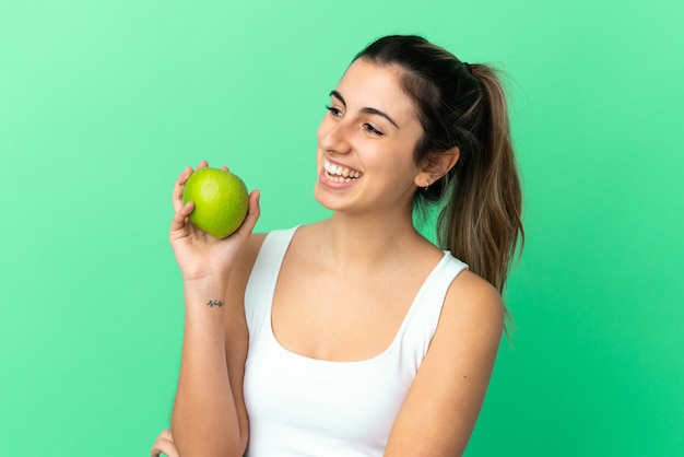 Joven mujer caucásica aislada sobre fondo verde con una manzana y feliz