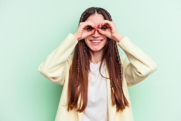 Joven mujer caucásica aislada sobre fondo verde mostrando bien firmar sobre los ojos