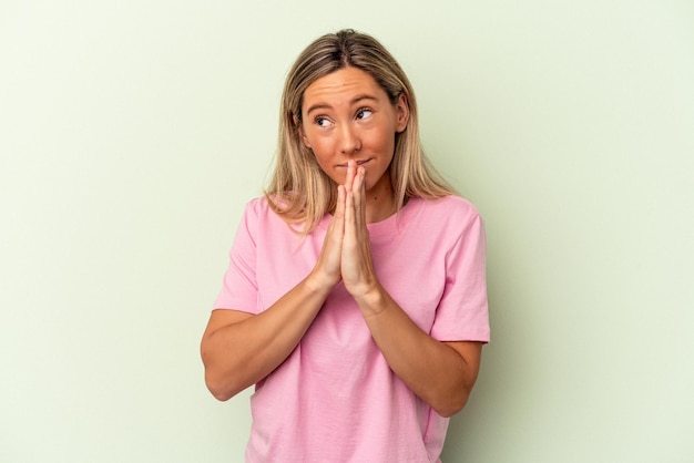 Joven mujer caucásica aislada sobre fondo verde rezando, mostrando devoción, persona religiosa en busca de inspiración divina.