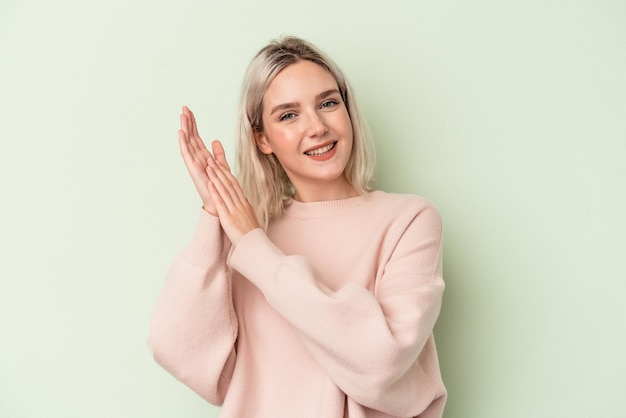 Joven mujer caucásica aislada sobre fondo verde sintiéndose enérgica y cómoda, frotándose las manos con confianza.